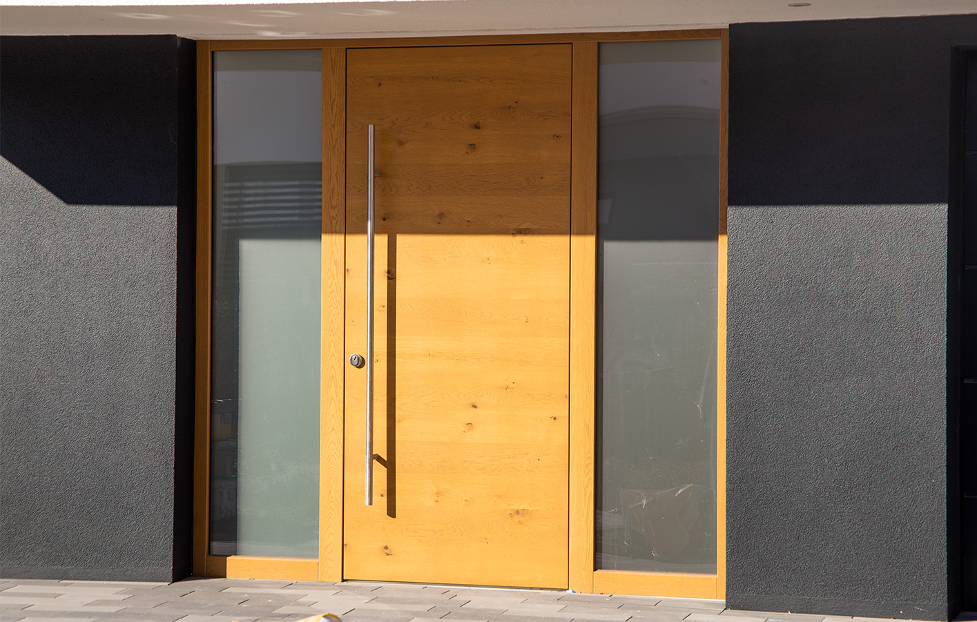 Dunkler Hauseingang mit heller Holzhaustür und seitlichen Glasflächen